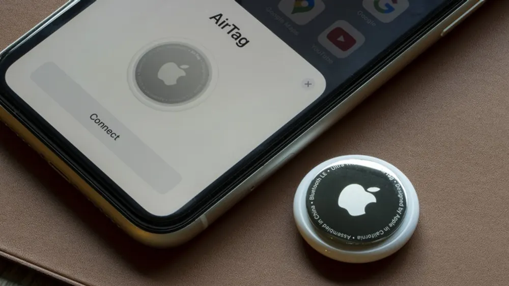 Apple AirTag Bluetooth tracking device alongside checked luggage and airline boarding pass on airport terminal floor
