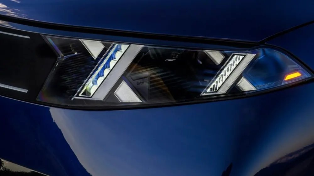 2027 BMW iX5 electric luxury SUV in Tanzanite Blue metallic on coastal highway showing front kidney grille