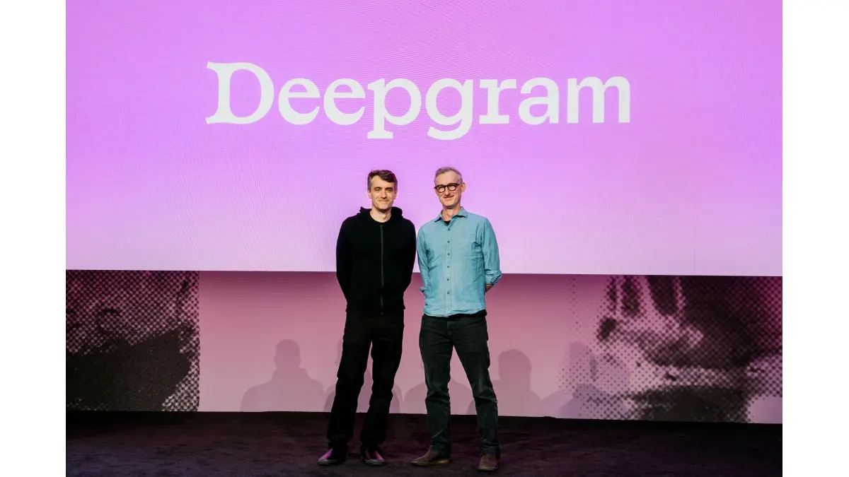 Two executives stand together on a stage in front of a large Deepgram display during a company presentation.