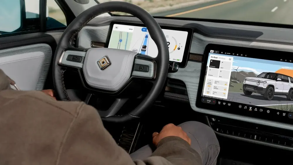 Interior view of a Rivian electric vehicle cockpit showing the digital dashboard and central infotainment display operating Universal Hands-Free assisted driving navigation across an open highway