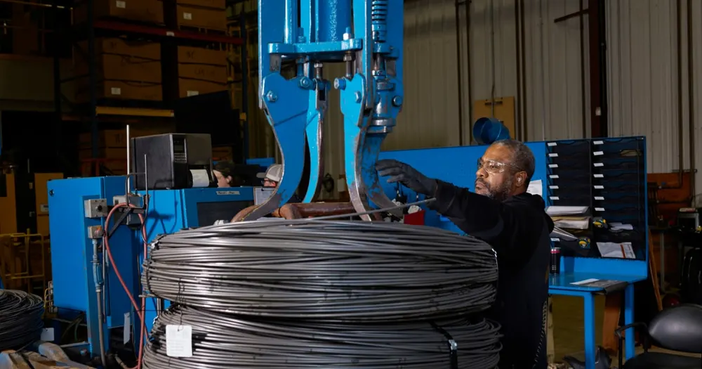 Authentic factory photograph of a Perryman Company technician handling coiled aerospace-grade titanium wire under Apple's American Manufacturing Program